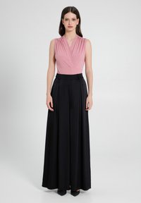 Top rosa senza maniche con scollatura a V plissettata e sottili scintillii, abbinato a pantaloni neri a gamba larga con vita alta.