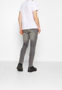 Gray slim-fit jeans with subtle fading, paired with a plain white t-shirt and black ankle boots, viewed from the back.