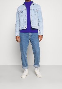 Ljusblå denimjacka med två bröstfickor över en lila långärmad skjorta. Bärs med avslappnade ljusblå jeans och vita sneakers.