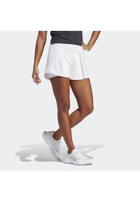 Pantalones cortos deportivos blancos con diseño plegado, textura suave y cinturilla de media altura, combinados con zapatillas deportivas blancas.