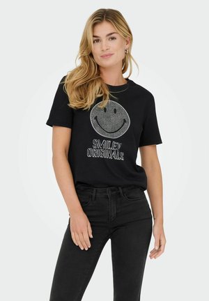 T-shirt noir avec un grand graphique de visage souriant blanc et le texte "SMILEY ORIGINALS" en dessous. Le modèle porte un jean noir taille haute.