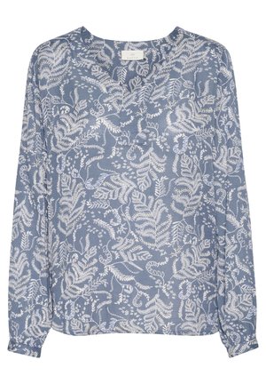 Blouse bleu à col en V avec des motifs blancs complexes de feuilles et de vignes, portée par une personne aux cheveux bouclés avec une main visible près de la taille.