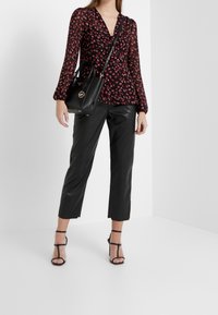 Halenka s květinovým vzorem v černé a červené barvě s dlouhými rukávy, spárovaná s černými zkrácenými kalhotami z umělé kůže s vysokým pasem a černými sandály na podpatku.