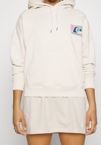 Sudadera crema con un bolsillo frontal, puños y dobladillo acanalados; cuenta con un colorido logo de Quiksilver en el lado izquierdo del pecho. Material de algodón suave.