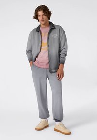 Chaqueta gris con botones a presión sobre una camiseta gráfica rosa; pantalones deportivos grises; zapatillas; texturas suaves, diseño casual.