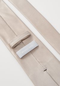 Cravate tissée beige en tissu texturé, dotée d'une boucle pour l'ajustement et d'une étiquette gris clair avec "MICHAEL KORS" en lettres blanches.
