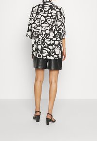 Svart och vit tryckt skjorta med abstrakta mönster, korta ärmar och rundad nederkant, tillsammans med svarta lädershorts och klacksandaler.