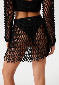 Copertura nera all'uncinetto con un design a maglia caratterizzato da strisce allungate e dettagli a nodo, completata da un top aderente e accenti triangolari.