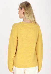 Geel gebreid sweater met lange mouwen, een ronde halslijn en een ontspannen pasvorm. De textuur lijkt zacht met een licht donzige afwerking.