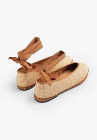 Ballerine in paglia intrecciata con una fascia alla caviglia in tessuto beige, punta tondeggiante e superficie testurizzata. Presenta una suola marrone per maggiore stabilità.