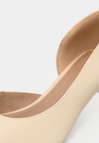 Μπεζ ψηλοτάκουνο παπούτσι με υφή, λεία επιφάνεια, στρογγυλεμένη μύτη και μαλακό εσωτερικό. Χωρίς ορατό εξάρτημα ή διακοσμητικά.