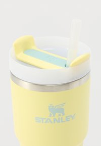 Gobelet isotherme jaune avec base en acier inoxydable, couvercle blanc et paille réutilisable. Le dessus est équipé d'un bouchon en silicone bleu clair.