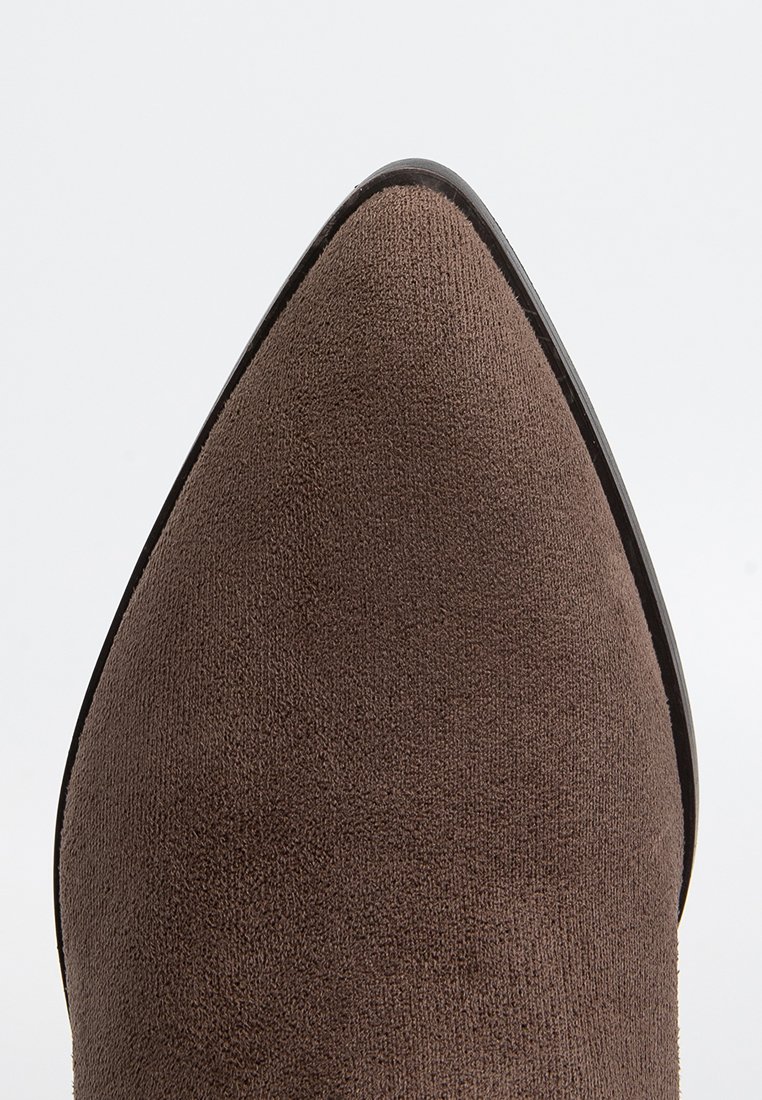 Scarpa in camoscio marrone con punta affusolata, superficie liscia, bordi neri e una silhouette elegante e slanciata.