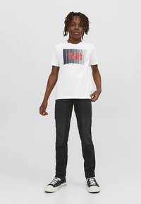 Camiseta blanca con diseño gráfico de rayas azules y rojas con el texto "JACK & JONES", combinada con jeans oscuros y zapatillas negras.