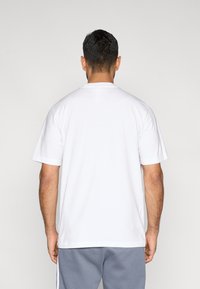 Valge puuvillane lühikeste varrukatega t-särk, ümmarguse kaelusega, tagantvaates. Sile tekstuur, lihtne disain, nähtavad mustrid puuduvad.