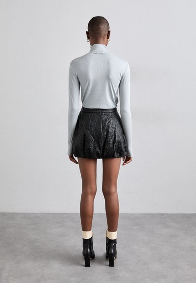Un haut à manches longues de couleur bleu clair associé à une mini jupe noire texturée et brodée, complété par des bottines noires à talons hauts.
