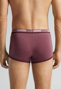 Bóxers burdeos con una cinturilla de contraste que presenta el nombre de la marca "Intimissimi". Tejido suave y diseño ajustado con bordes rematados.