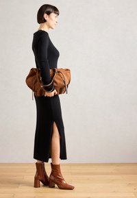 Vestido negro de manga larga con relieve y abertura lateral, combinado con un bolso de ante marrón. Botas de tobillo brillantes marrones con puntera cuadrada y tacones de bloque.