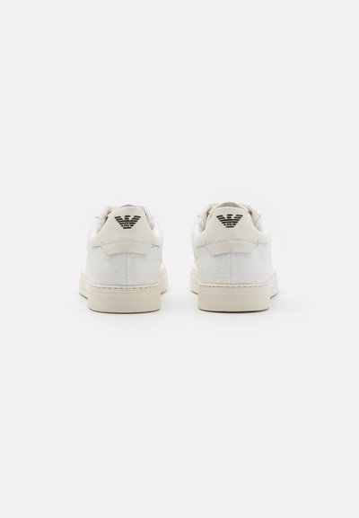 White sneakers with a textured upper, cream rubber sole, and logo detail on the heel. Designed for casual wear with minimalistic style.