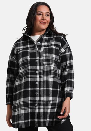 Chemise à carreaux en flanelle noire et blanche avec un col, des manches longues et une fermeture à boutons, dotée d'une poche à l'avant et d'un tissu doux et texturé.