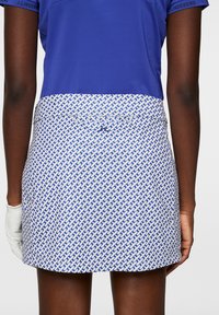 Blå polo med kort �ärm i kombination med en vit kjol med ett blått geometriskt mönster och en bakfickdesign.