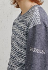 Sudadera de punto con rayas horizontales en azul y blanco, manga raglán en azul oscuro y logotipo bordado de "Missoni" en la manga.