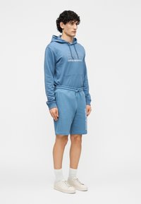 Blå bomulls-hoodie med framficka, matchad med blå shorts med elastisk midja och logotypdetalj på sidan.