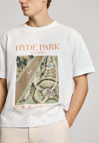 Witte katoenen t-shirt met een gekleurd ontwerp van Hyde Park, Londen, met oranje tekst en verfijnde details van het park. Korte mouwen, ontspannen pasvorm.