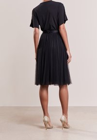 Abito nero con un top liscio e gonna in tulle, caratterizzato da una vita aderente. Abbinato a tacchi alti dorati luccicanti.