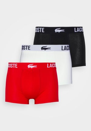 Trois paires de boxers Lacoste en rouge, blanc et noir. Chacune présente une taille élastique avec logo contrastant. Matière en coton stretch.