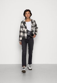 Zwart-witte geruite jas, getailleerd wit shirt, donkere jeans en zilveren veterschoenen. Accessoires zijn onder andere een zwarte schoudertas met een ketting.