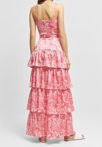 Robe maxi rose à fleurs avec plusieurs niveaux de volants, fines bretelles et corsage ajusté. Le tissu a une texture douce et un motif vibrant.