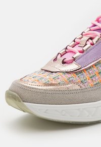 Gros plan sur l’avant d’une basket multicolore avec des lacets roses, un détail en daim violet, une tige en tissu tissé et une semelle beige clair.