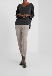 Schwarzes, V-Ausschnitt Langarmoberteil, kombiniert mit karierter Hose in Rot, Grün und Beige. Das Model trägt knöchelhohe, strukturierte grüne Stiefel.