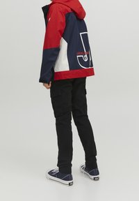 Punainen, laivastonsininen ja valkoinen värieste takki hupulla; siinä on suuri logo ja cargo-tyyliset housut, jotka on yhdistetty laivastonsinisiin lenkkitossuihin.