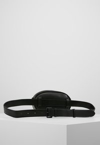 Svart läder bältesväska med oval form, platt front och justerbart band. Har en minimalistisk design utan synliga hårdvarudetaljer.