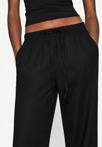 Black linen pants with an elastic waistband and drawstring. Features side pockets, loose fit, and a textured fabric.