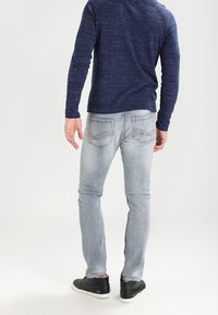 Jean en denim bleu clair à coupe ajustée, avec deux poches arrière ornées de coutures. Assorti à une chemise à manches longues bleu foncé.
