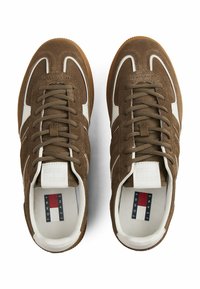 Sneaker scamosciati marroni con un design a strisce bianche, punta rotonda e lacci in tessuto testurizzato. Branding visibile sulle solette. Suole in gomma.
