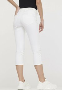 Jean capri blancs en tissu extensible, avec une taille mi-haute, des poches arrière et une coupe ajustée, associés à des baskets blanches.