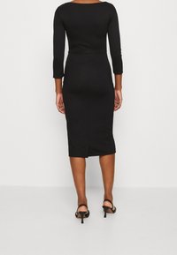 Musta, kapea mekko, jossa on kolmivartiset hihat, polven pituinen, sileä tekstuuri, hienovarainen takareikä, yhdistetty mustiin hihnaosa kenkäihin.