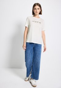 T-shirt à manches courtes gris clair avec le texte "new york city". Associé à un jean bleu large et à des baskets crème. Design simple, coupe décontractée.