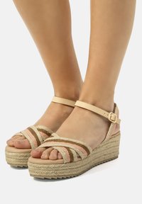 Sandalias de cuña al estilo espadrille con correas de tejido trenzado en rosa, beige y marrón; plataforma de yute; correa al tobillo con hebilla dorada.