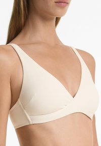 Lichtbeige driehoekige bralette met brede bandjes en textuurstof. Het V-halsontwerp heeft een kruislingse voorkant en een zachte onderband.