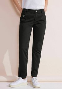 Svarta tapered byxor i bomull med ficka med dragkedja, kombinerade med vita sneakers. Slät yta och enkel design.