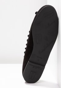 Ballerine en daim noir avec une semelle texturée. Caractérisée par un design à lacets et un logo en relief sur la semelle. Taille 37.