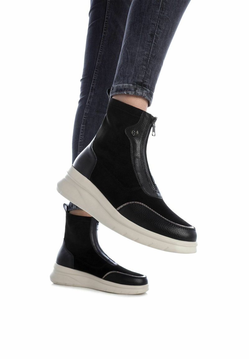 Des bottines noires présentent un mélange de daim et de cuir, une fermeture éclair et une épaisse semelle blanche. Le design comprend des accents texturés et des coutures.