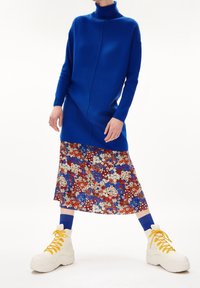 Blå stickad polotröja, blommönstrad midijurk i rött, vitt och blått, kombinerad med kraftiga vita sneakers och blå strumpor.