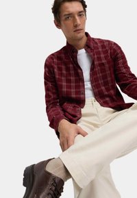 Bordeaux geruite shirt over een wit T-shirt, gecombineerd met crèmekleurige broeken en bruine veterschoenen, met een soepele textuur en een relaxte pasvorm.