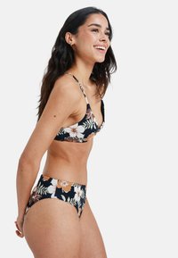 Kvetinová súprava bikín na čiernom pozadí s bielymi a oranžovými kvetmi. Tričko má tenké ramienka a trojuholníkový tvar, nohavičky sú s vysokým pásom.